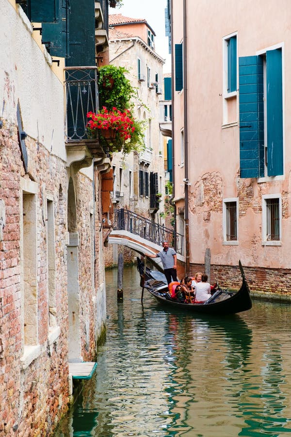 Turister som rider en gondol på en liten kanal som omges av gamla byggnader i Venedig arkivfoton Turister som rider en gondol på en liten kanal som omges av gamla byggnader i Venedig arkivfoton