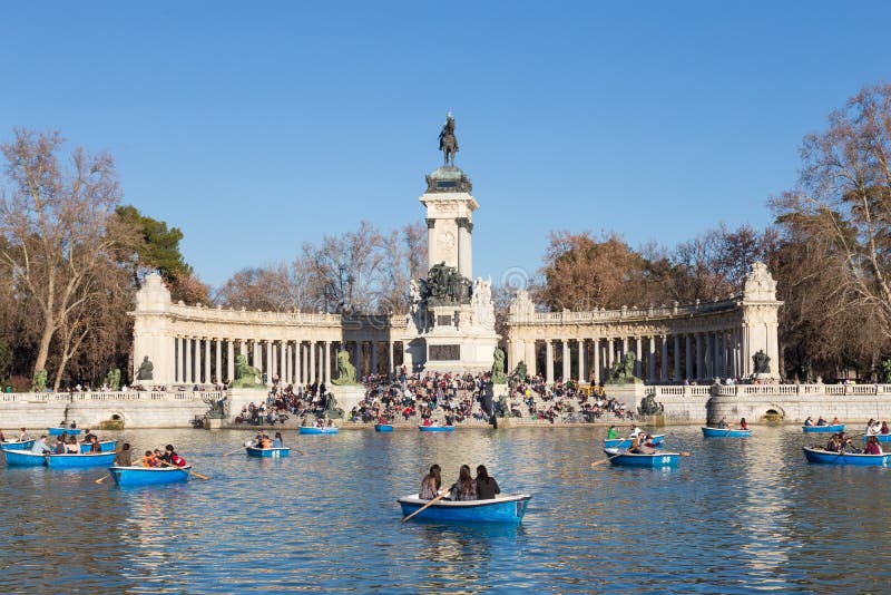 Turister som ror traditionella blåa fartyg på sjön i den Retiro staden, parkerar på en trevlig solig vinterdag i Madrid, Spanien royaltyfria bilder Turister som ror traditionella blåa fartyg på sjön i den Retiro staden, parkerar på en trevlig solig vinterdag i Madrid, Spanien royaltyfria bilder