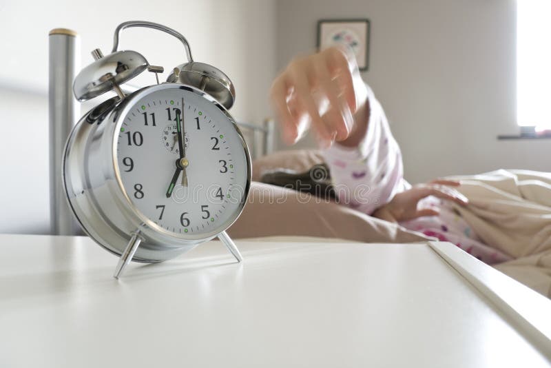 Young woman turning off alarm clock, motion blur on hand to exaggerate action, white copy space beneath