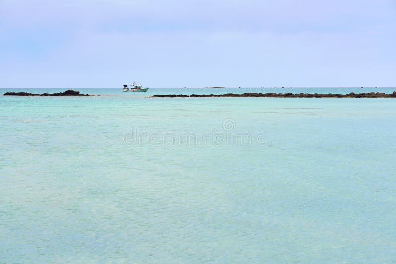 Turquoise blue sea water on a lagoon with a ship on a horizon line ander a cloudy sky. Copy space.