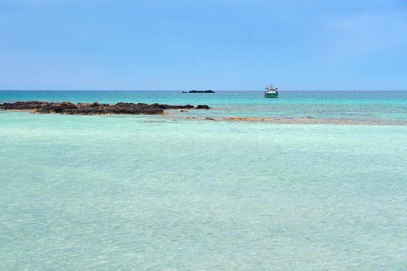 Turquoise blue sea water on a lagoon with a ship on a horizon line ander a cloudy sky. Copy space.