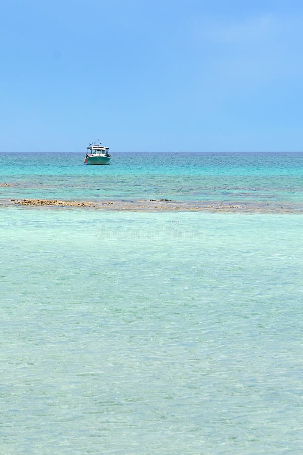 Turquoise blue sea water on a lagoon with a ship on a horizon line ander a cloudy sky. Copy space.