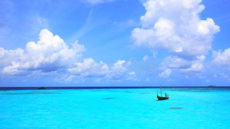 Panorama delle acque turchesi della laguna in Maldive con una piccola barca e belle nuvole.