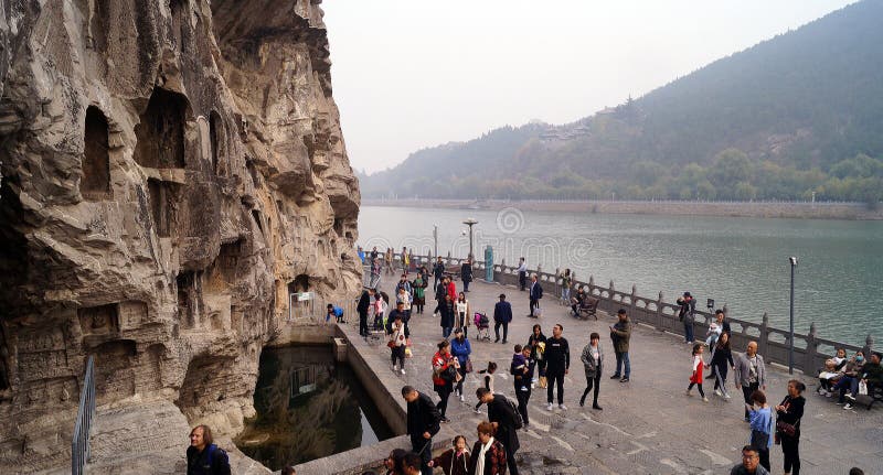 Longmen grottoes with several niches carved in the wall at the face of a mountain, buddhist temple whit several sculptures in it, tourists passing by. Longmen grottoes with several niches carved in the wall at the face of a mountain, buddhist temple whit several sculptures in it, tourists passing by