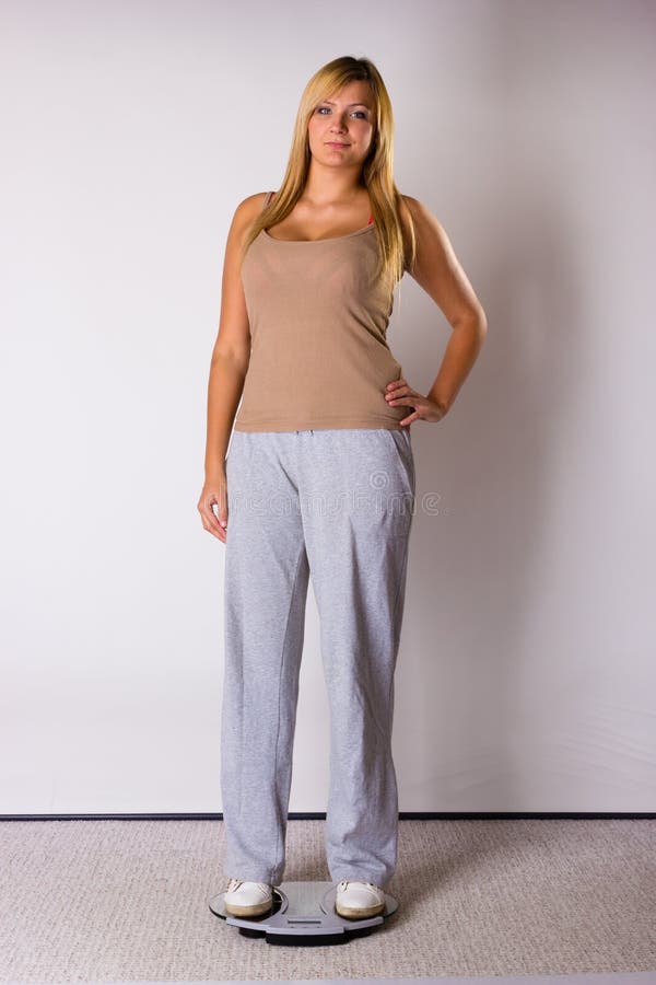 Tuta sportiva d'uso della donna felice che sta sulla bascula fotografia stock Tuta sportiva d'uso della donna felice che sta sulla bascula fotografia stock