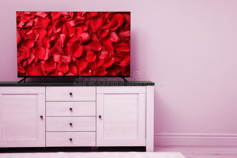 TV screen with red rose petals on commode near pink wall in room, space for text