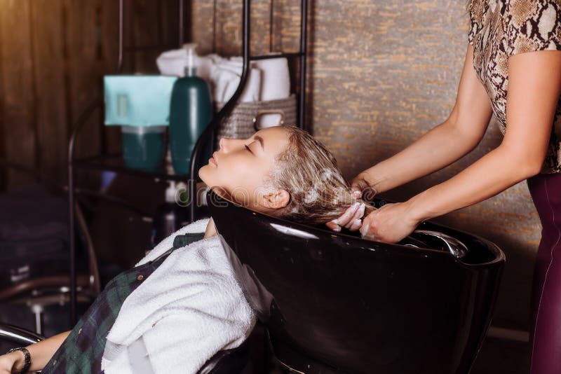 Beautiful woman washing hair in a hair salon. Hair stylist washing hair to the customer before doing hairstyle. Hairdresser applying nourishing mask on woman`s hair in beauty salon. Hair wash shampoo, hair care products, spa