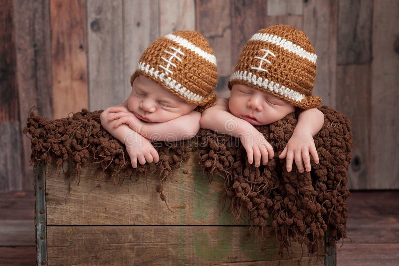 Four week old fraternal, twin, newborn baby boys sleeping in a vintage, wooden crate and wearing football shaped caps. Shot in the studio on a wood background. Four week old fraternal, twin, newborn baby boys sleeping in a vintage, wooden crate and wearing football shaped caps. Shot in the studio on a wood background.