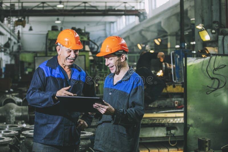 Två arbetare på en industrianläggning med en minnestavla i handen, workin arkivfoto Två arbetare på en industrianläggning med en minnestavla i handen, workin arkivfoto