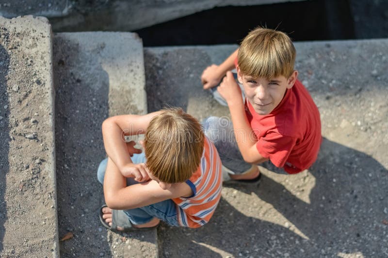 Två barn sitter på trappan av en övergiven byggnad av ett koncept för gatubarnens eller föräldralösa barns liv arkivfoton