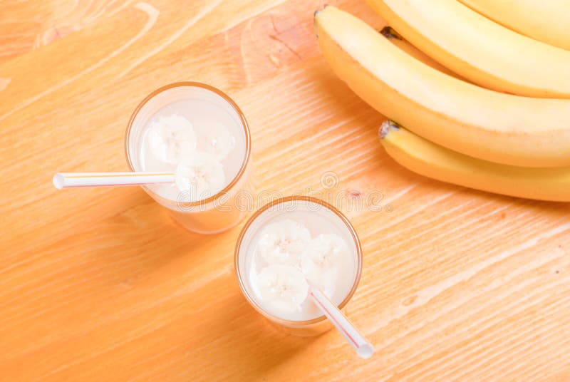 Två exponeringsglas av bananfruktsaft på tabellen bredvid ett gult moget b arkivfoton Två exponeringsglas av bananfruktsaft på tabellen bredvid ett gult moget b arkivfoton