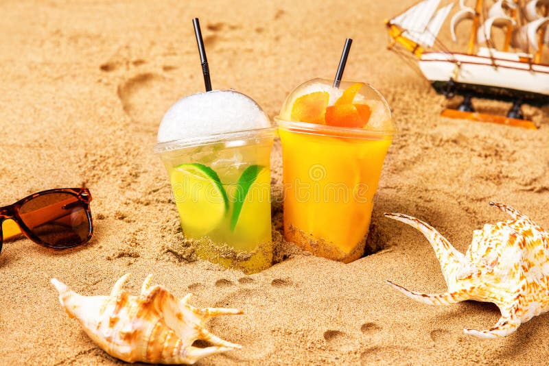 Två exponeringsglas av nya coctailar på gul strandsand med seashel arkivbild Två exponeringsglas av nya coctailar på gul strandsand med seashel arkivbild