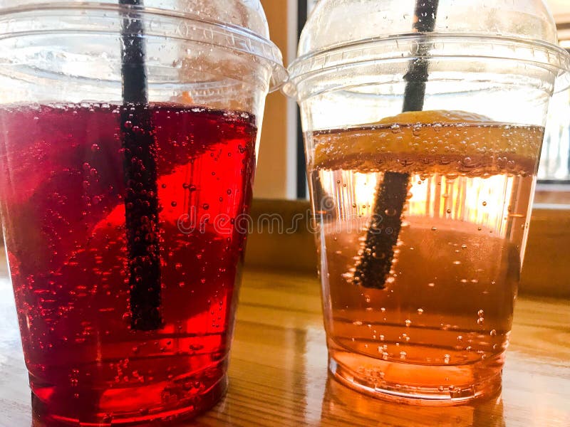 Två exponeringsglas av plast- lemonad för frukt för citron för persika för röd och gul uppfriskande kall smaklig söt hallonjordgu arkivfoton
