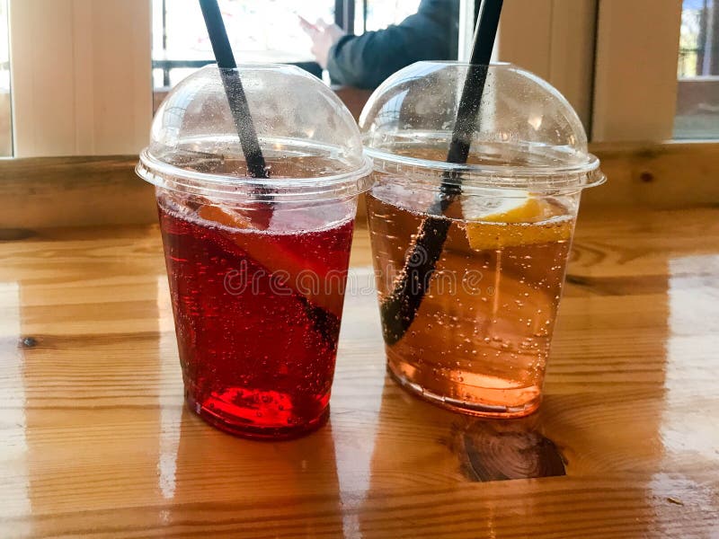 Två exponeringsglas av plast- lemonad för frukt för citron för persika för röd och gul uppfriskande kall smaklig söt hallonjordgu royaltyfria foton