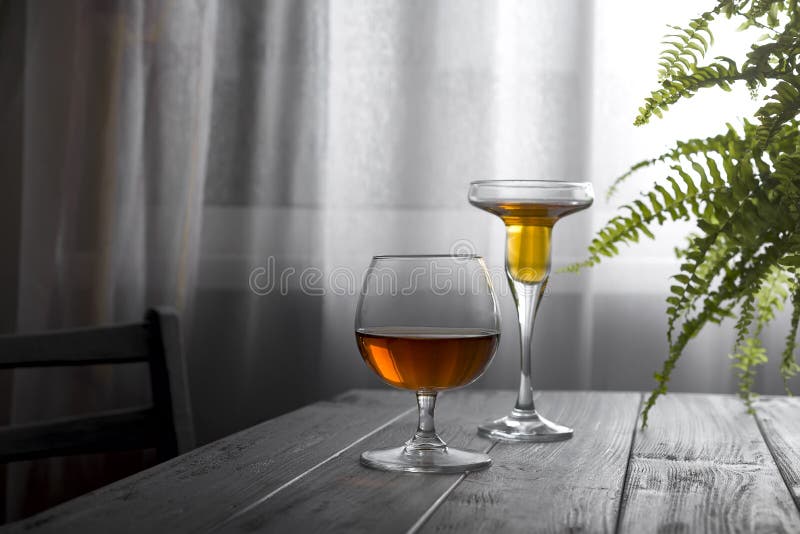 Två exponeringsglas av vin som förläggas på en trätabell på bakgrunden av ett fönster med en vit gardin Naturligt ljus från a arkivfoto Två exponeringsglas av vin som förläggas på en trätabell på bakgrunden av ett fönster med en vit gardin Naturligt ljus från a arkivfoto
