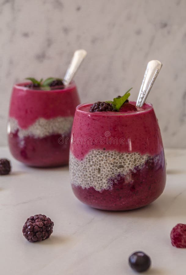 Två exponeringsglas som fylls med den i lager den blåbärhallonsmoothien & mandeln, mjölkar chiapudding med silverskedar mot den v fotografering för bildbyråer Två exponeringsglas som fylls med den i lager den blåbärhallonsmoothien & mandeln, mjölkar chiapudding med silverskedar mot den v fotografering för bildbyråer