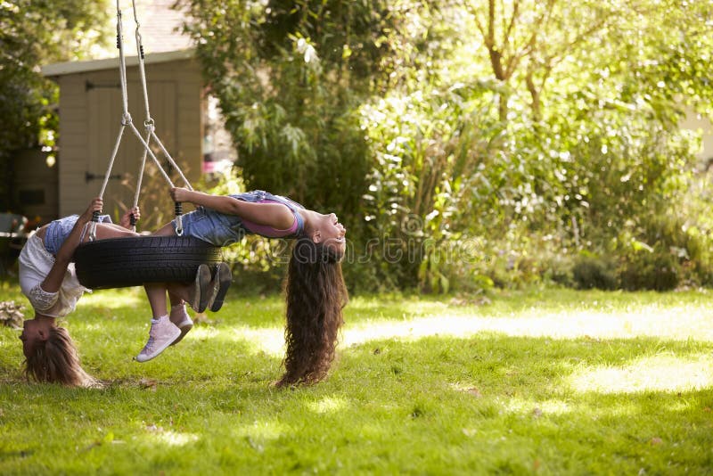 Two Girls Playing Together On Tire Swing In Garden. Two Girls Playing Together On Tire Swing In Garden