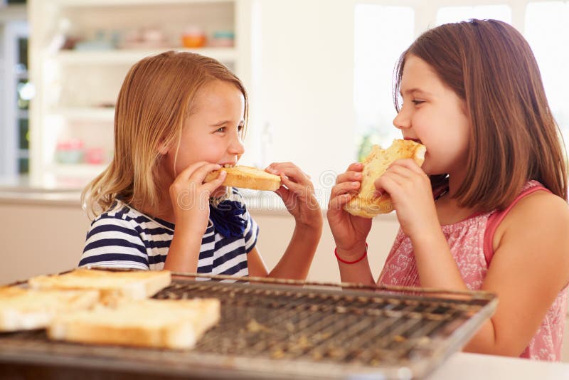 Two Girls Eating Cheese On Toast In Kitchen. Two Girls Eating Cheese On Toast In Kitchen