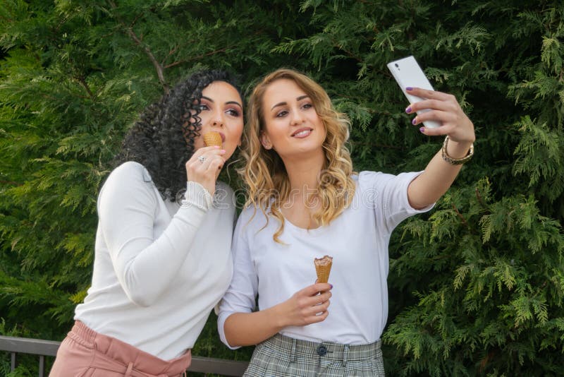 Två flickor tar selfies och äter glass royaltyfri bild Två flickor tar selfies och äter glass royaltyfri bild