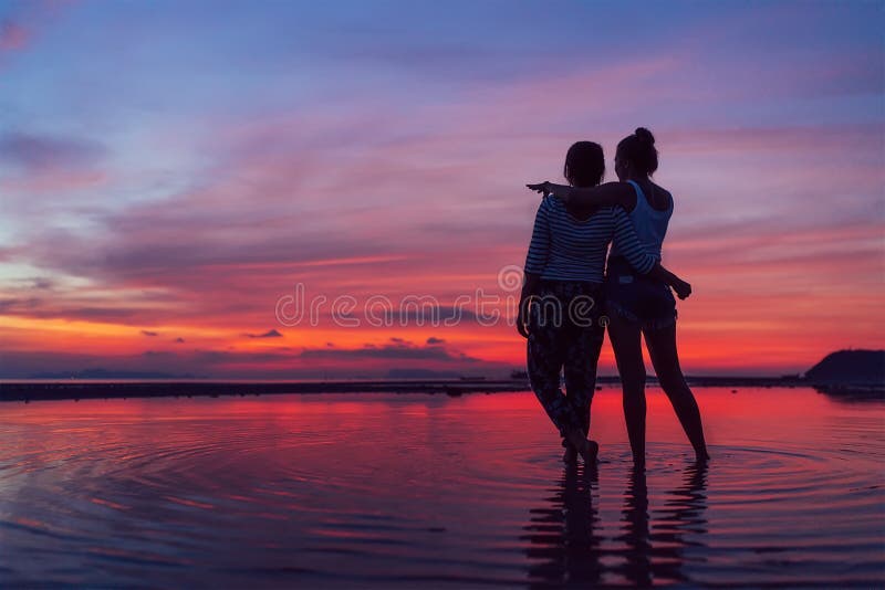 Två flickvänner som kramar och njuter av en rosa/rosa solsken på havsstranden på Samui Island i Thailand Värmeländer fotografering för bildbyråer Två flickvänner som kramar och njuter av en rosa/rosa solsken på havsstranden på Samui Island i Thailand Värmeländer fotografering för bildbyråer