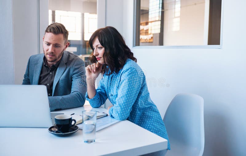 Två fokuserade businesspeople som arbetar på en bärbar dator i ett kontor royaltyfria foton Två fokuserade businesspeople som arbetar på en bärbar dator i ett kontor royaltyfria foton