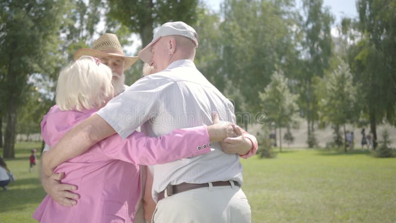 Två förtjusande mogna par som kramar i, parkerar tillsammans att stå i cirkel Dubbelträff av höga par v?nskapsmatch