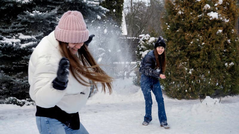 Två glada skrattande tonårsflickor som spelar snöbullar på bakgården på snövintern. människor som leker utomhus under vintersemest arkivbild