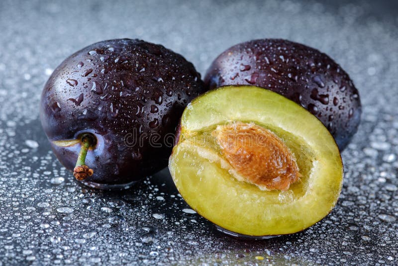 Två hela och plommoner för halvan skivade krikon med stenen på en svart skärbräda med vatten tappar Makro som skjutas av nytt, or arkivbild Två hela och plommoner för halvan skivade krikon med stenen på en svart skärbräda med vatten tappar Makro som skjutas av nytt, or arkivbild