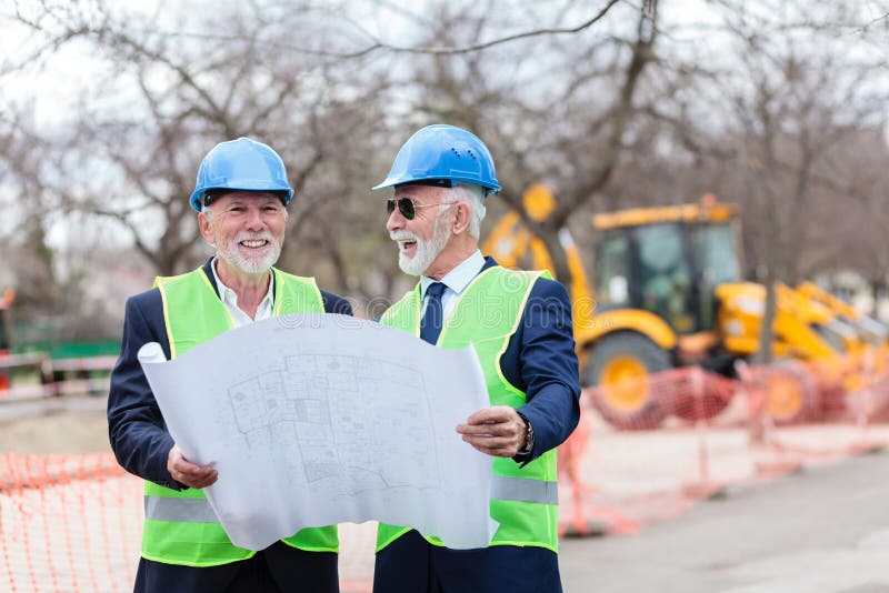 Två höga arkitekter eller affärspartners som besöker konstruktionsplatsen som ser byggnadsritningar royaltyfri fotografi Två höga arkitekter eller affärspartners som besöker konstruktionsplatsen som ser byggnadsritningar royaltyfri fotografi