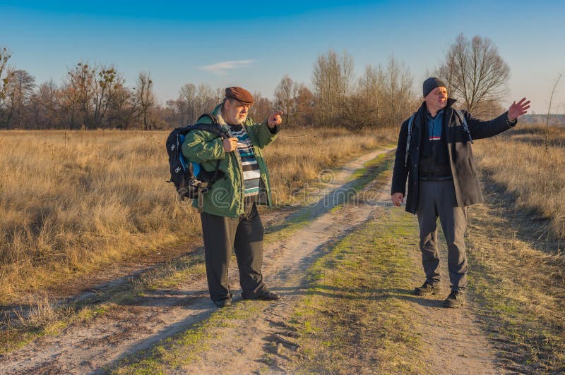 Två höga fotvandrare med ryggsäckar som diskuterar den korrekta banan, medan gå på en landsväg fotografering för bildbyråer Två höga fotvandrare med ryggsäckar som diskuterar den korrekta banan, medan gå på en landsväg fotografering för bildbyråer
