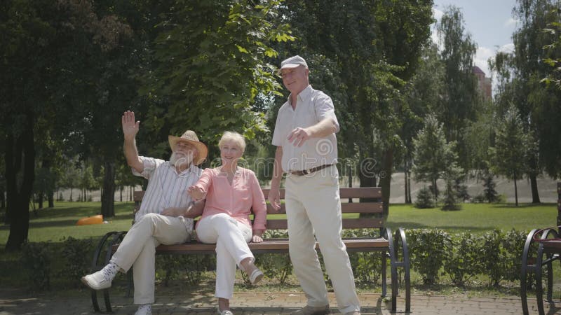 Två höga män och vinkande händer för en kvinna i parkerar Moget folk som vilar det fria, aktiv livsstil gladlynt pension?r