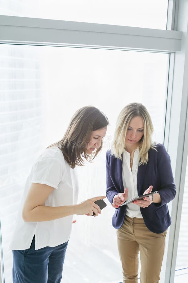Två kvinnliga coworkers som använder mobiltelefonen royaltyfri bild Två kvinnliga coworkers som använder mobiltelefonen royaltyfri bild