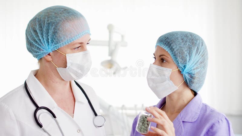 Två kvinnliga doktorer i medicinska maskeringar som diskuterar ny behandling på sjukhusrum Hållande flaska av preventivpillerar