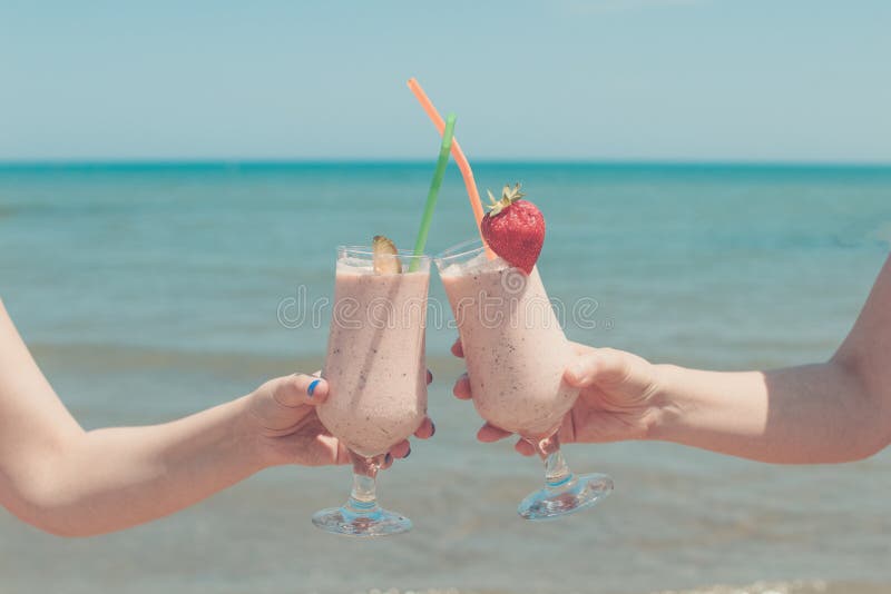 Två kvinnliga händer rymmer jordgubbemilkshakar på bakgrunden av havet fotografering för bildbyråer Två kvinnliga händer rymmer jordgubbemilkshakar på bakgrunden av havet fotografering för bildbyråer