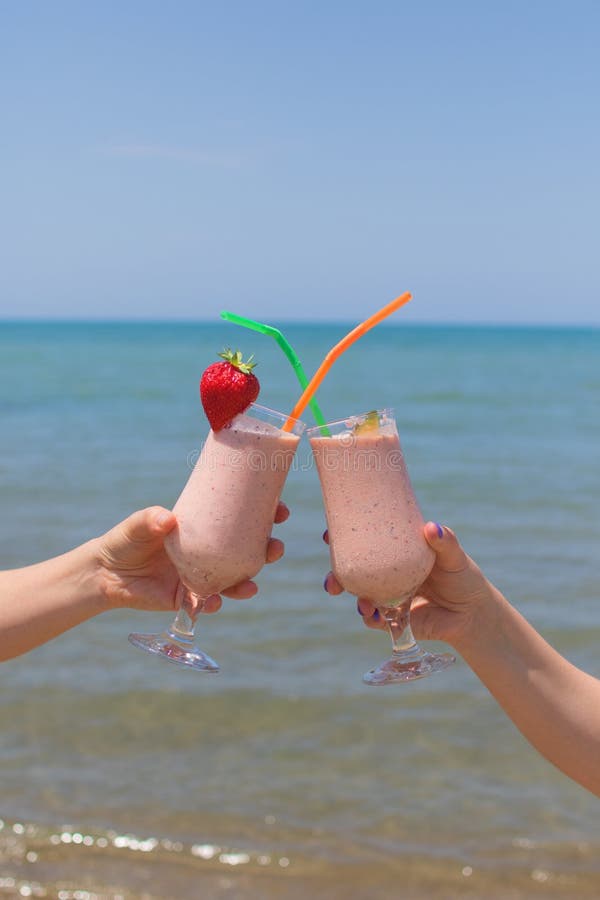 Två kvinnliga händer rymmer jordgubbemilkshakar på bakgrunden av havet royaltyfri foto Två kvinnliga händer rymmer jordgubbemilkshakar på bakgrunden av havet royaltyfri foto