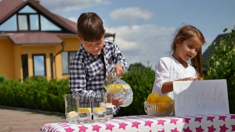 Två lilla ungar säljer lemonad på en hemlagad lemonadställning på en solig dag med ett pristecken för en entreprenör