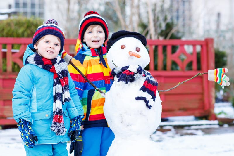 Två lilla vänner som gör en snögubbe, spelar och har gyckel med royaltyfri foto Två lilla vänner som gör en snögubbe, spelar och har gyckel med royaltyfri foto