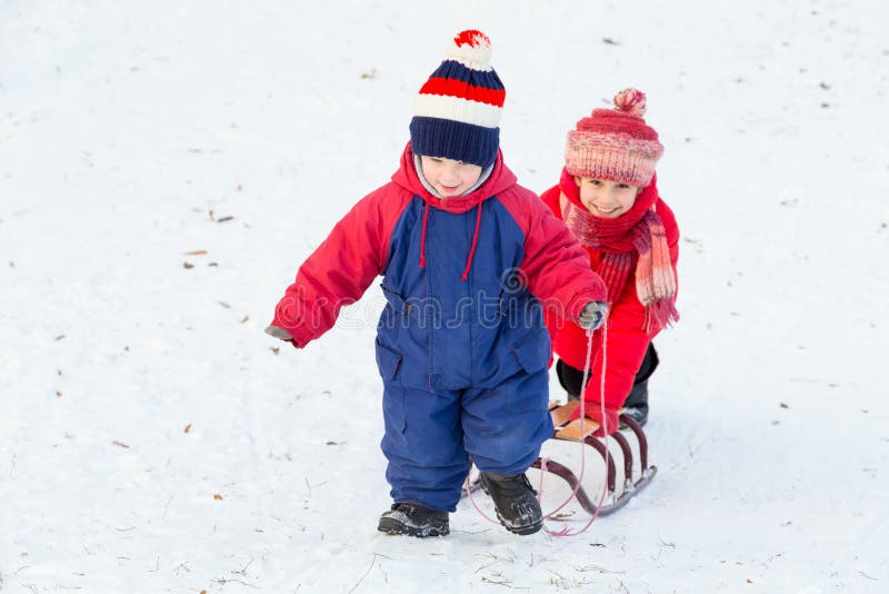 Två lyckliga ungar med släden som går på snö, sluttar royaltyfri foto Två lyckliga ungar med släden som går på snö, sluttar royaltyfri foto