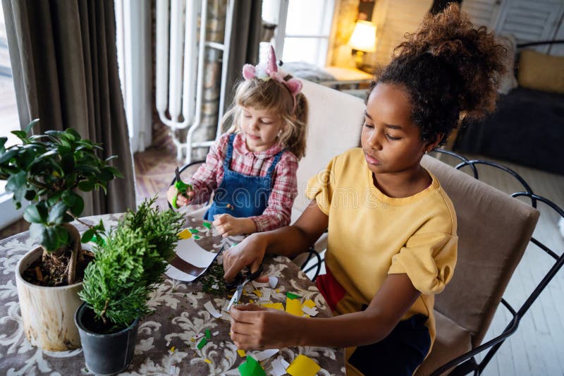 Två multietniska barn håller på att plantera husplantor hemma med trädgårdsverktyg. royaltyfri bild