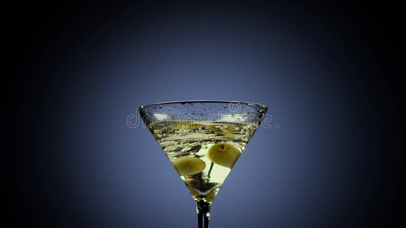 Två oliv faller in i högväxt martini exponeringsglas Svart bakgrund