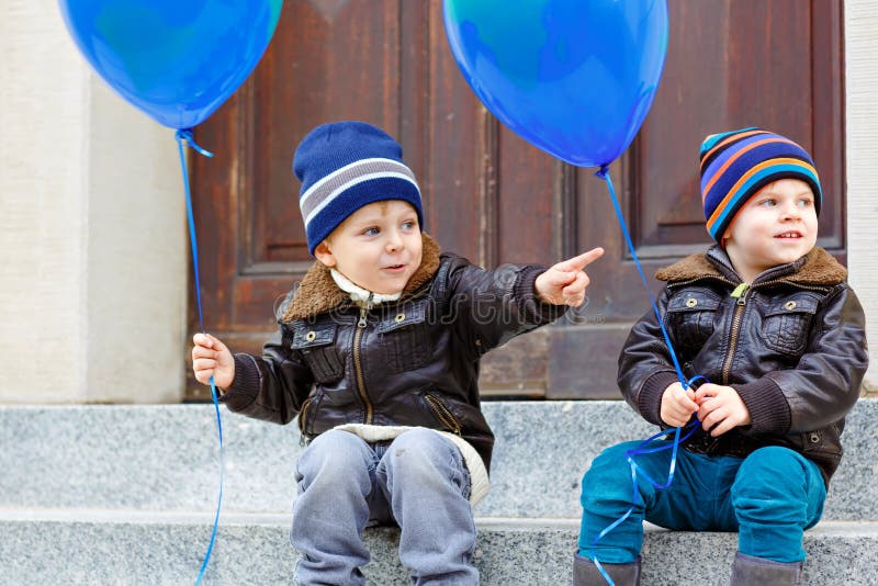 Två pojkar för små ungar som spelar med ballonger för blå luft utomhus Lyckligt kopplar samman och litet barnbröder som ler och s royaltyfri bild Två pojkar för små ungar som spelar med ballonger för blå luft utomhus Lyckligt kopplar samman och litet barnbröder som ler och s royaltyfri bild