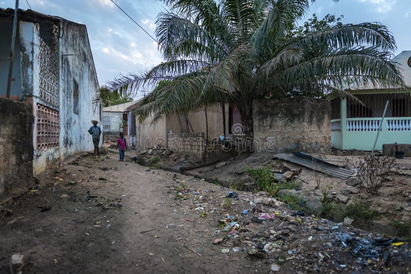 Två pojkar som går i en smutsgata längs en öppen avklopp på den Cupelon de Baixo grannskapen i staden av Bissau arkivfoton Två pojkar som går i en smutsgata längs en öppen avklopp på den Cupelon de Baixo grannskapen i staden av Bissau arkivfoton