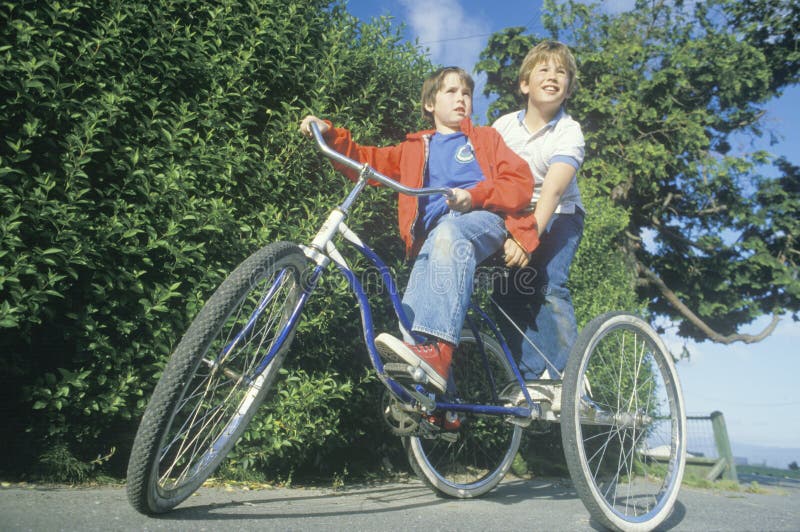 Två pojkar som rider en tre rullad cykel royaltyfria foton Två pojkar som rider en tre rullad cykel royaltyfria foton