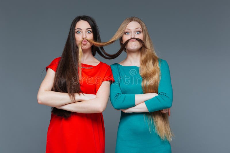 Två roliga flickor som gör mustaschen med deras hår royaltyfri foto Två roliga flickor som gör mustaschen med deras hår royaltyfri foto