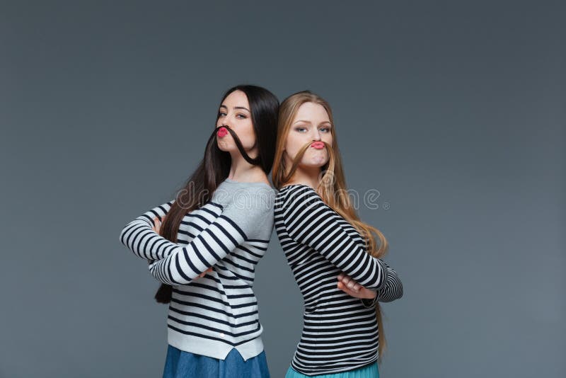 Två roliga unga kvinnor som gör mustaschen med deras hår arkivbilder Två roliga unga kvinnor som gör mustaschen med deras hår arkivbilder