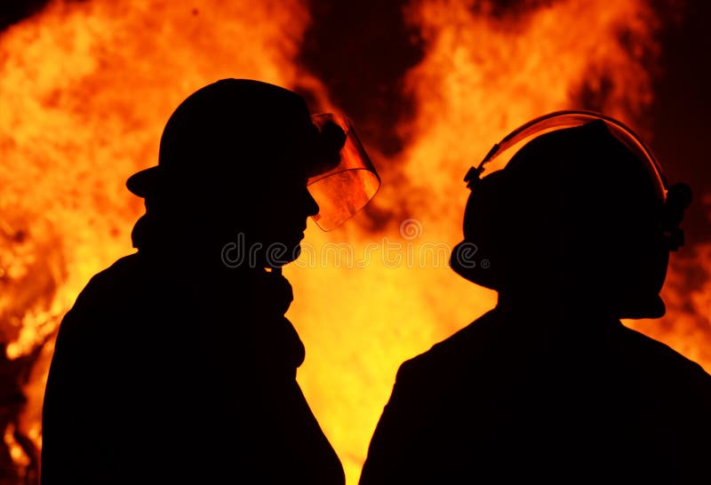 A striking silhouette image of two firemen called to an Australian bushfire blaze that started at night time. The men are discussing their plans for controlling the blazing flames. A striking silhouette image of two firemen called to an Australian bushfire blaze that started at night time. The men are discussing their plans for controlling the blazing flames.