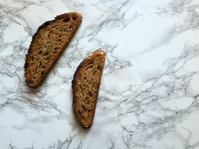 Två skivor av artisanal bröd för helt vete för sourdough på marmorcountertop arkivfoto Två skivor av artisanal bröd för helt vete för sourdough på marmorcountertop arkivfoto
