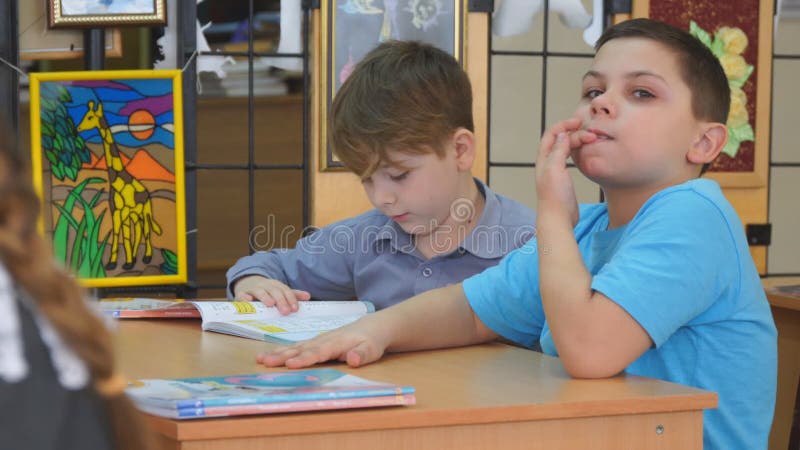 Två skolbarn sitter på skrivbordet med böcker. skolpojke biter sina naglar