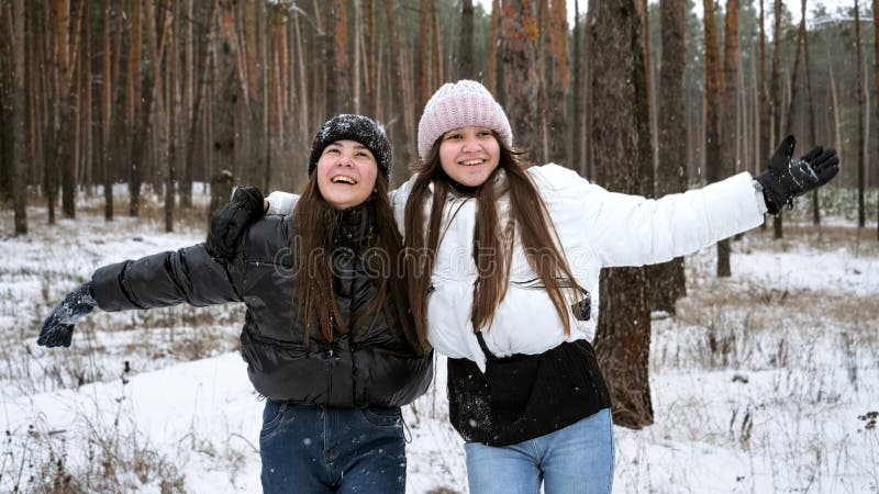 Två skrattande tonårsflickor som fuskar och skrattar medan de får sjunkande snöflingor i vinterskogen arkivbild