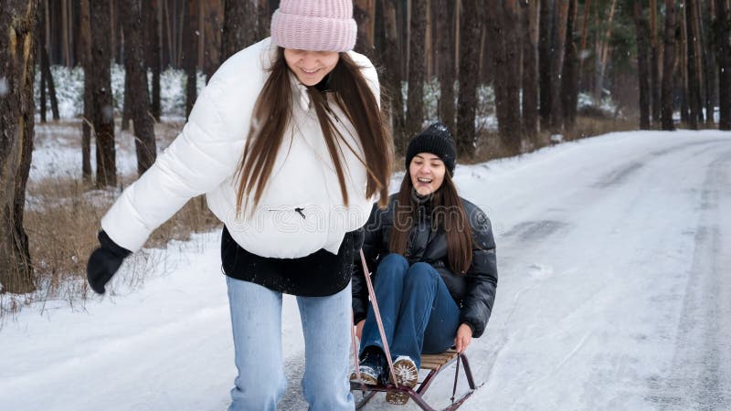 Två skrattande tonårsflickor som skrattar och har kul när de rider på sömnen i skogen. människor som leker utomhus under vintersem arkivfoton